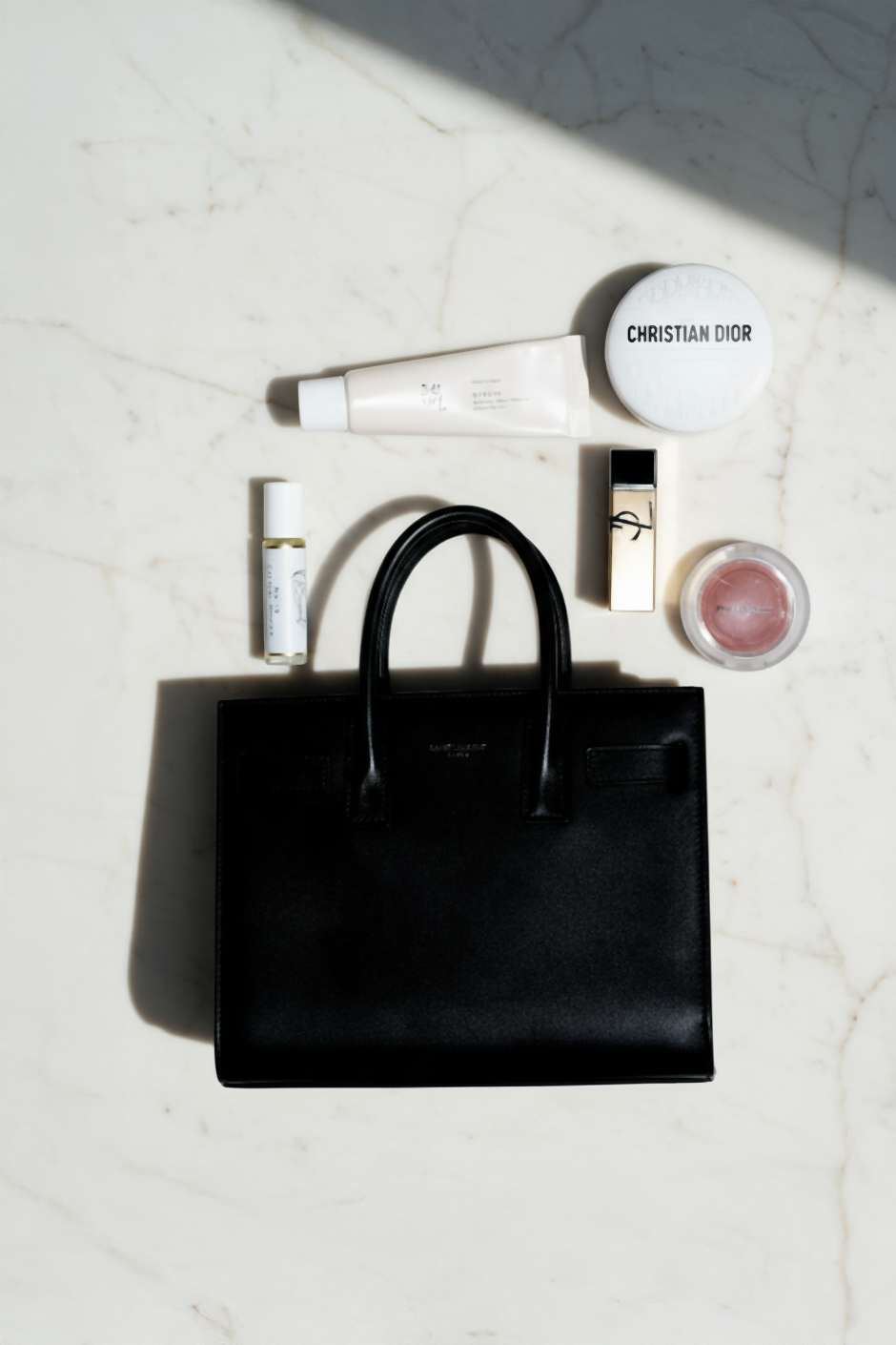 LeScent roll-on perfume oil styled with a black handbag and daily beauty essentials in a lifestyle flat lay.