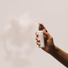 Hand holding and spraying LeScent Interior Fragrance bottle, releasing a fine mist against a neutral background.