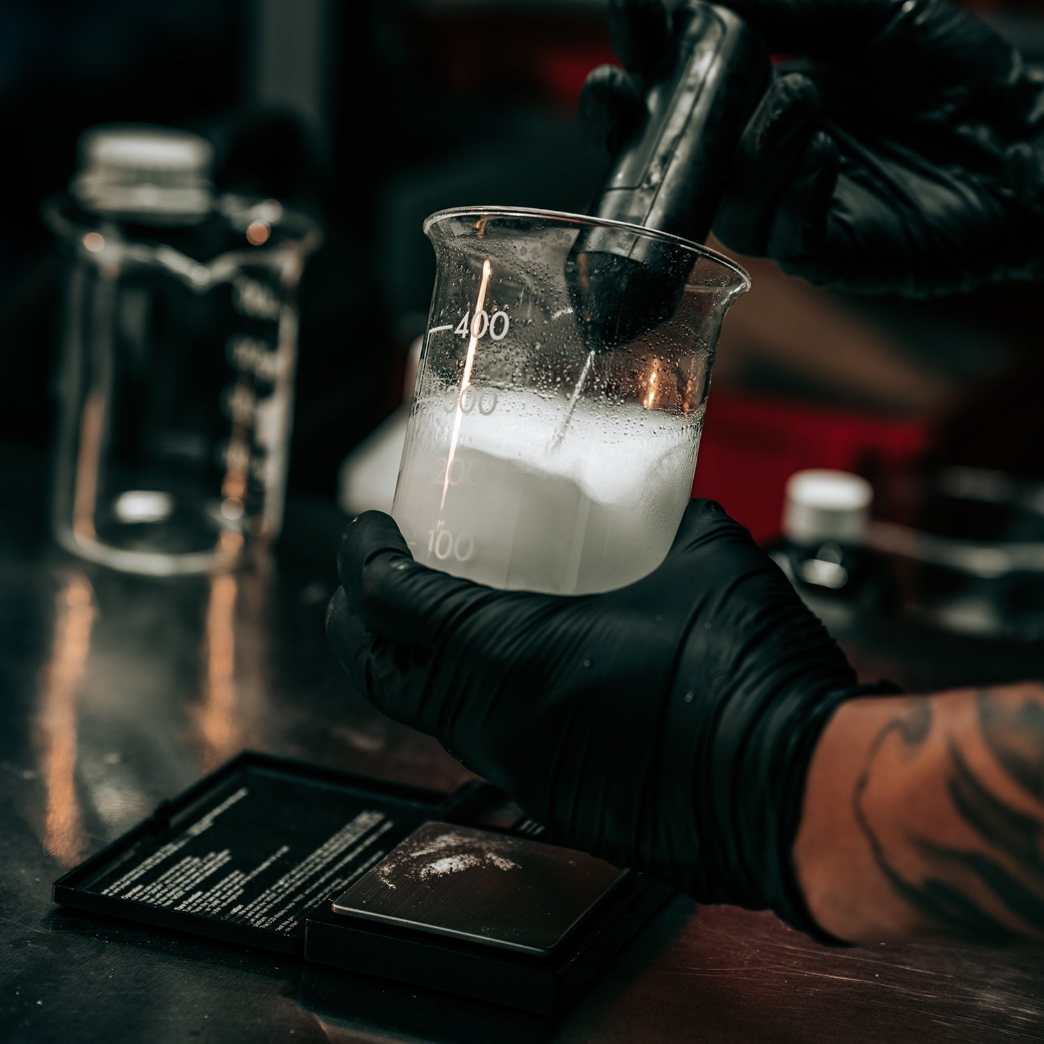 Gloved hands mixing fragrance ingredients in a beaker during the creation of a new perfume formula.