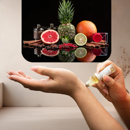 Applying LeScent Absoluta roll-on perfume oil surrounded by pineapple, grapefruit, lime, and cinnamon on a glossy black surface, inspired by Creed Aventus Absolu.