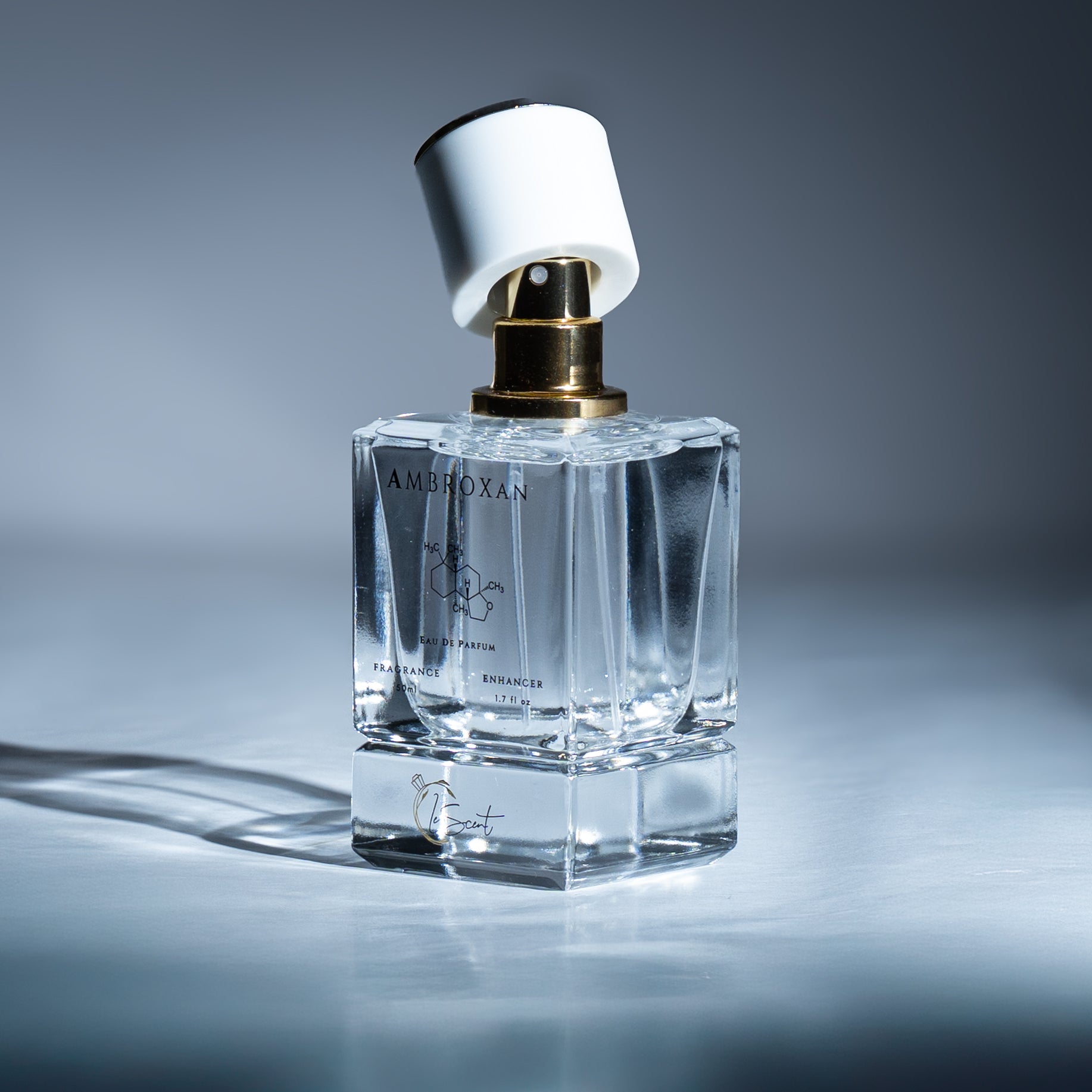 LeScent Ambroxan perfume bottle with gold sprayer and white cap illuminated under soft blue light, emphasizing its elegant and clean composition.