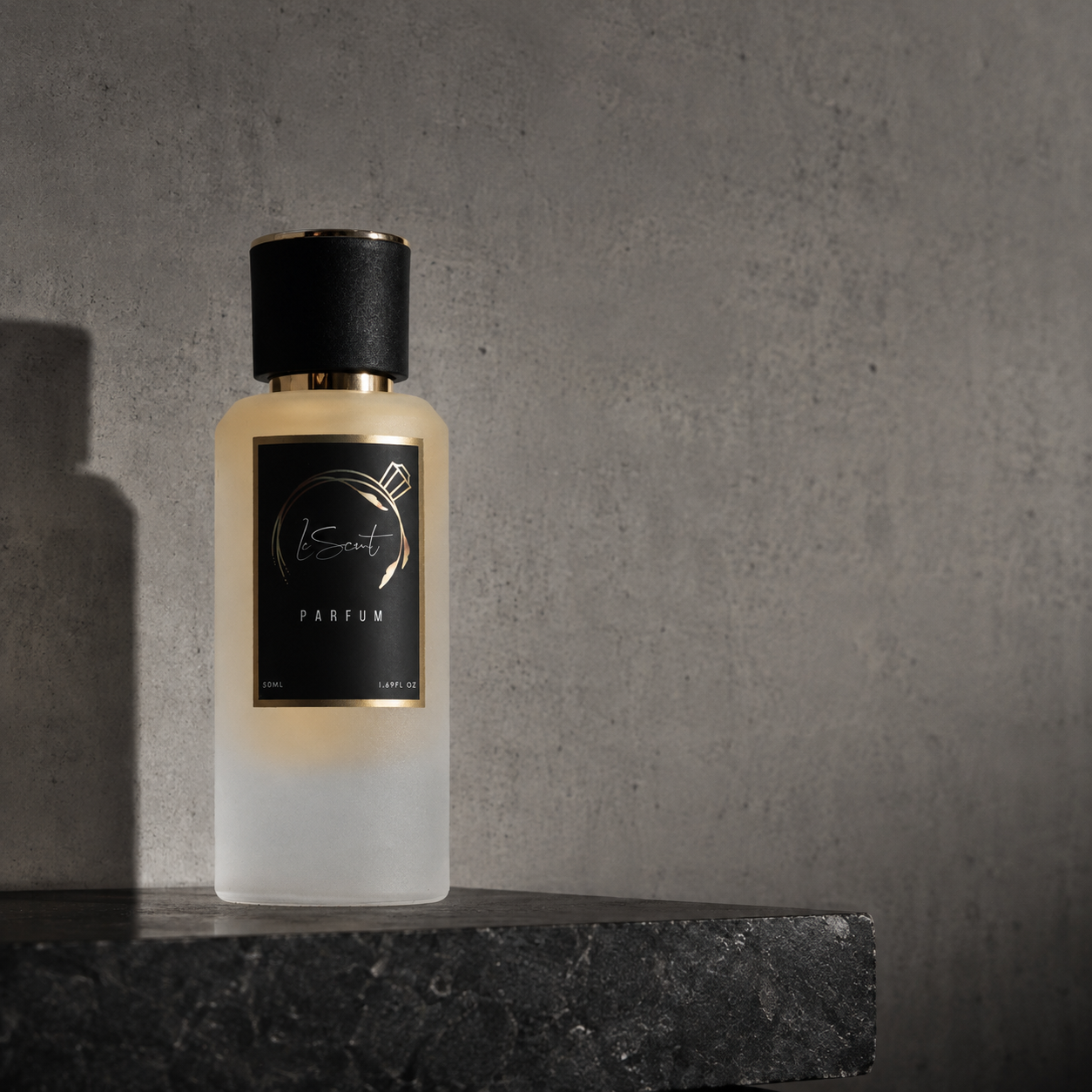 A frosted glass perfume bottle with a black cap and a black label featuring gold lettering, displayed on a dark stone surface against a textured gray concrete wall.