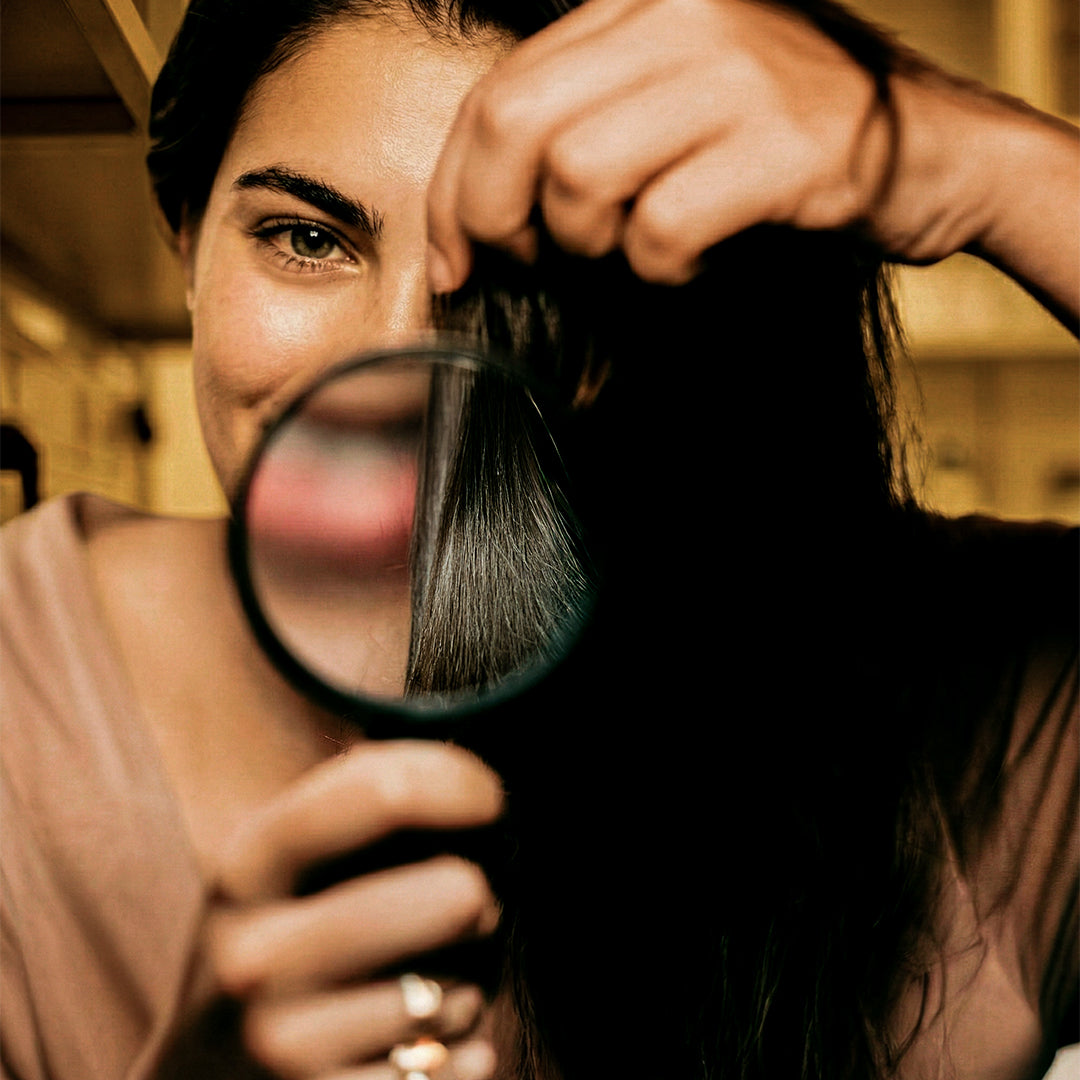 Close-up of a woman inspecting shiny hair strands with a magnifying glass, highlighting hair texture and smoothness for hair perfume, hair fragrance, and hair perfume mist.