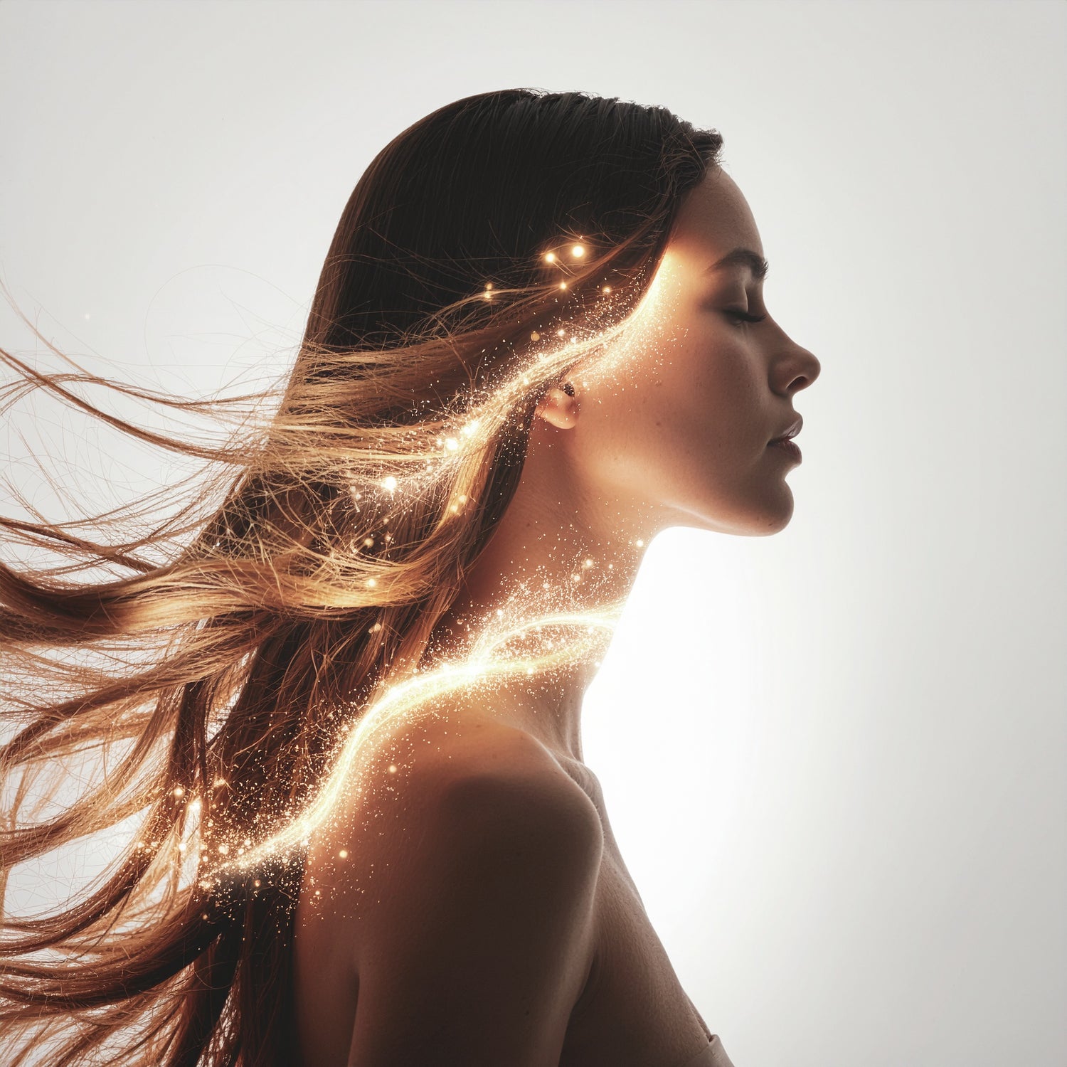 Elegant woman with luminous flowing hair surrounded by golden light particles, representing vitality and shine of LeScent Hair Mist.