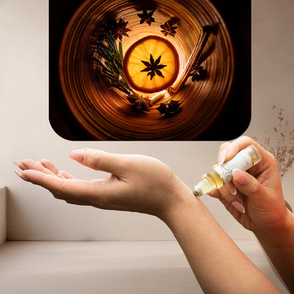 Applying LeScent Intense Homme roll-on perfume oil on wrist beside glowing orange slice, star anise, and rosemary on a neutral surface, inspired by Dior Homme Intense.