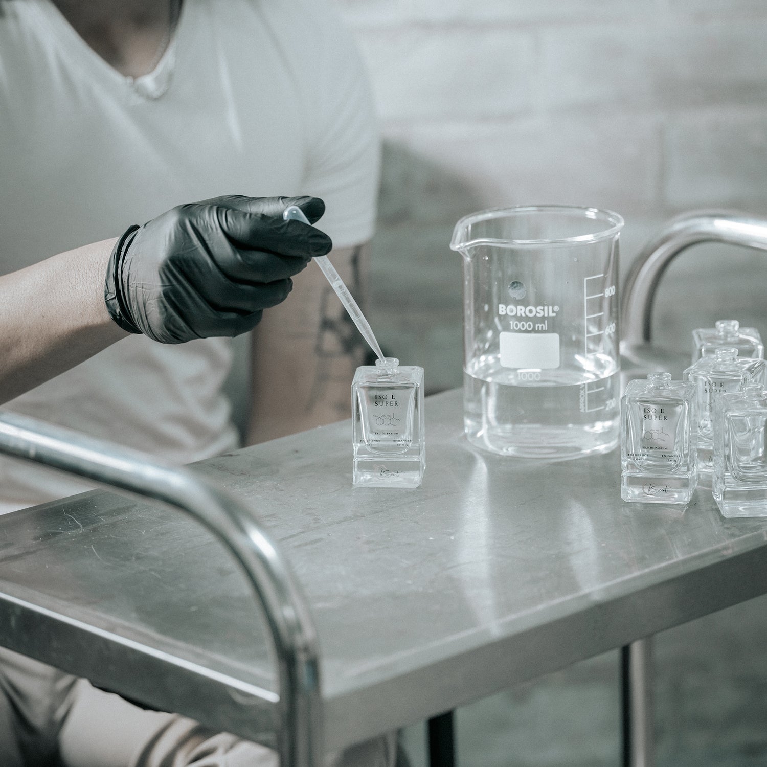 Perfumer using a dropper to fill ISO E Super bottles in a stainless steel lab, illustrating LeScent’s artisanal fragrance blending process.