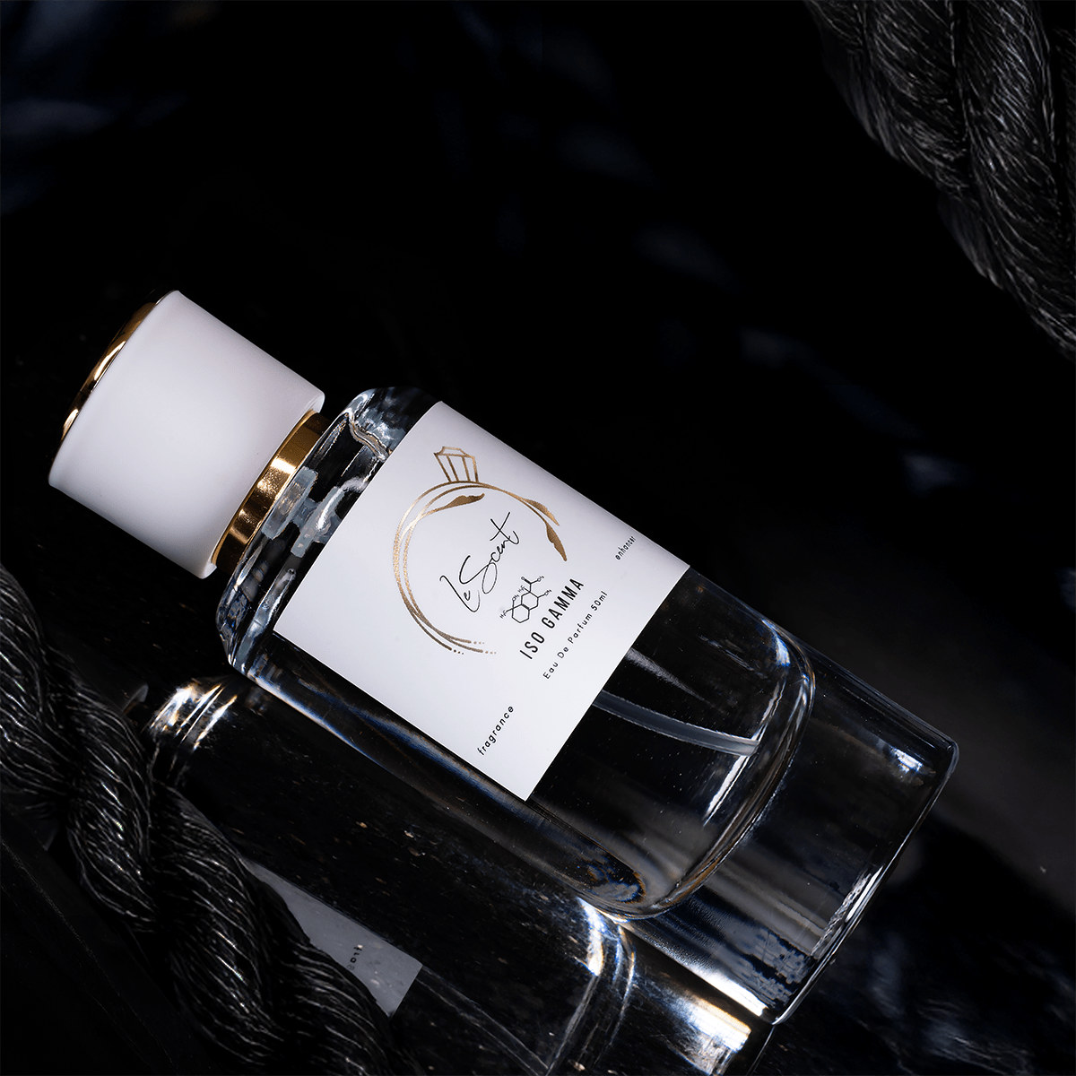 LeScent ISO Gamma Super perfume bottle with white cap and gold accent resting on a dark reflective surface beside textured rope, showcasing its luxurious design.
