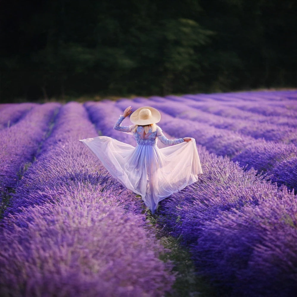 A woman in a white dress and straw hat walking through a vibrant purple lavender field, evoking a sense of natural fragrance.