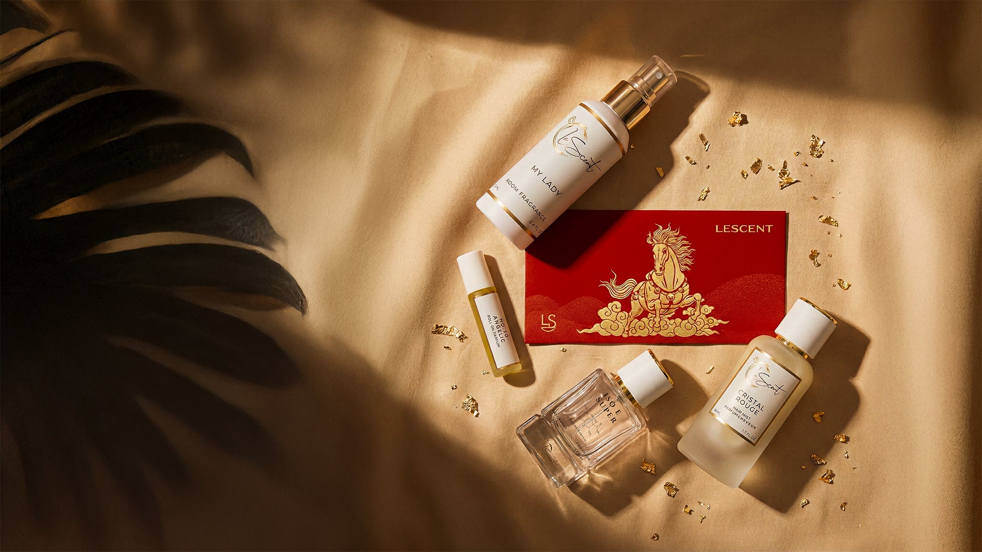 LeScent fragrance collection flat lay featuring My Lady room fragrance, Cristal Rouge hair mist, roll-on perfume oil, and perfume primer beside a red Lunar New Year envelope on golden satin.