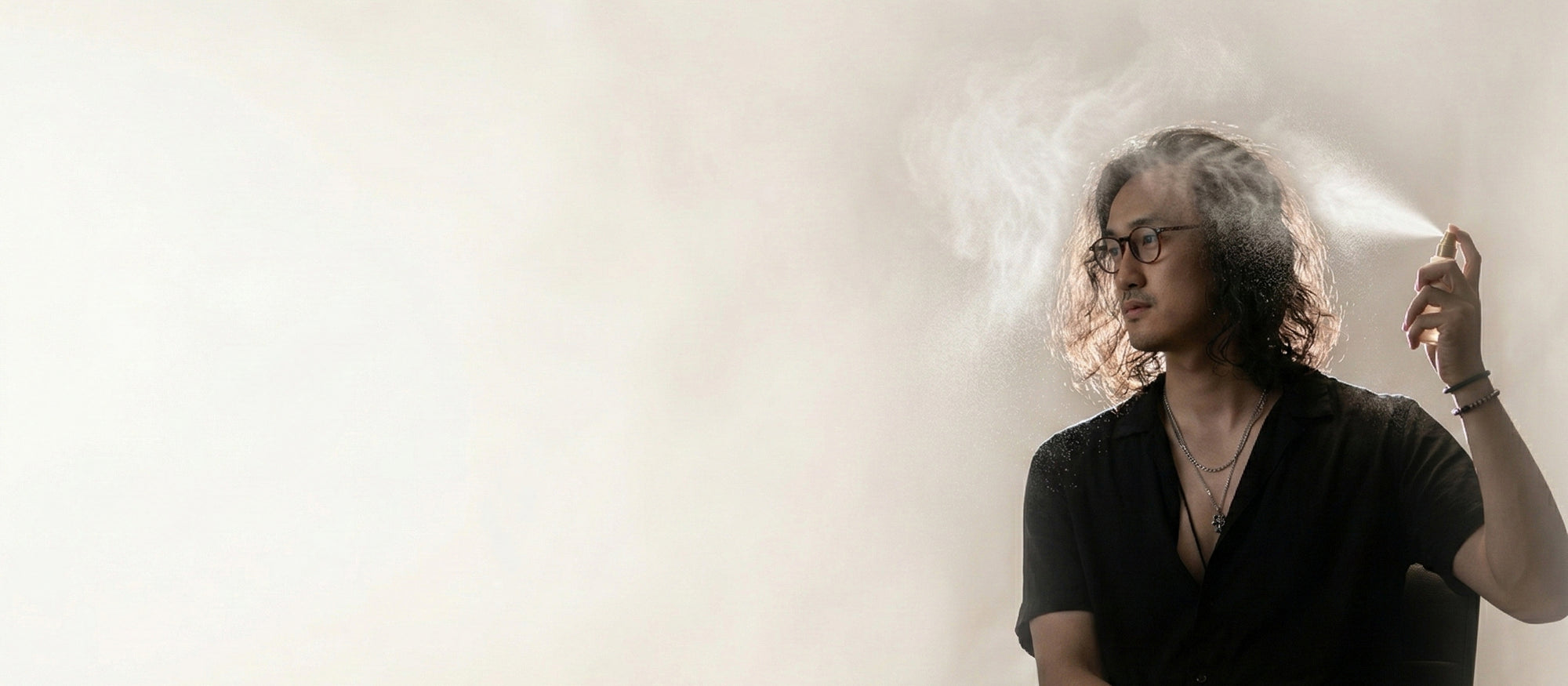 Man applying LeScent hair mist in a soft-lit editorial setting, with fine mist diffusing around his hair.