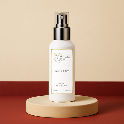 LeScent My Lady room fragrance spray bottle presented on a cream pedestal against a warm beige and red backdrop with subtle studio lighting, inspired by Frédéric Malle Portrait of a Lady.
