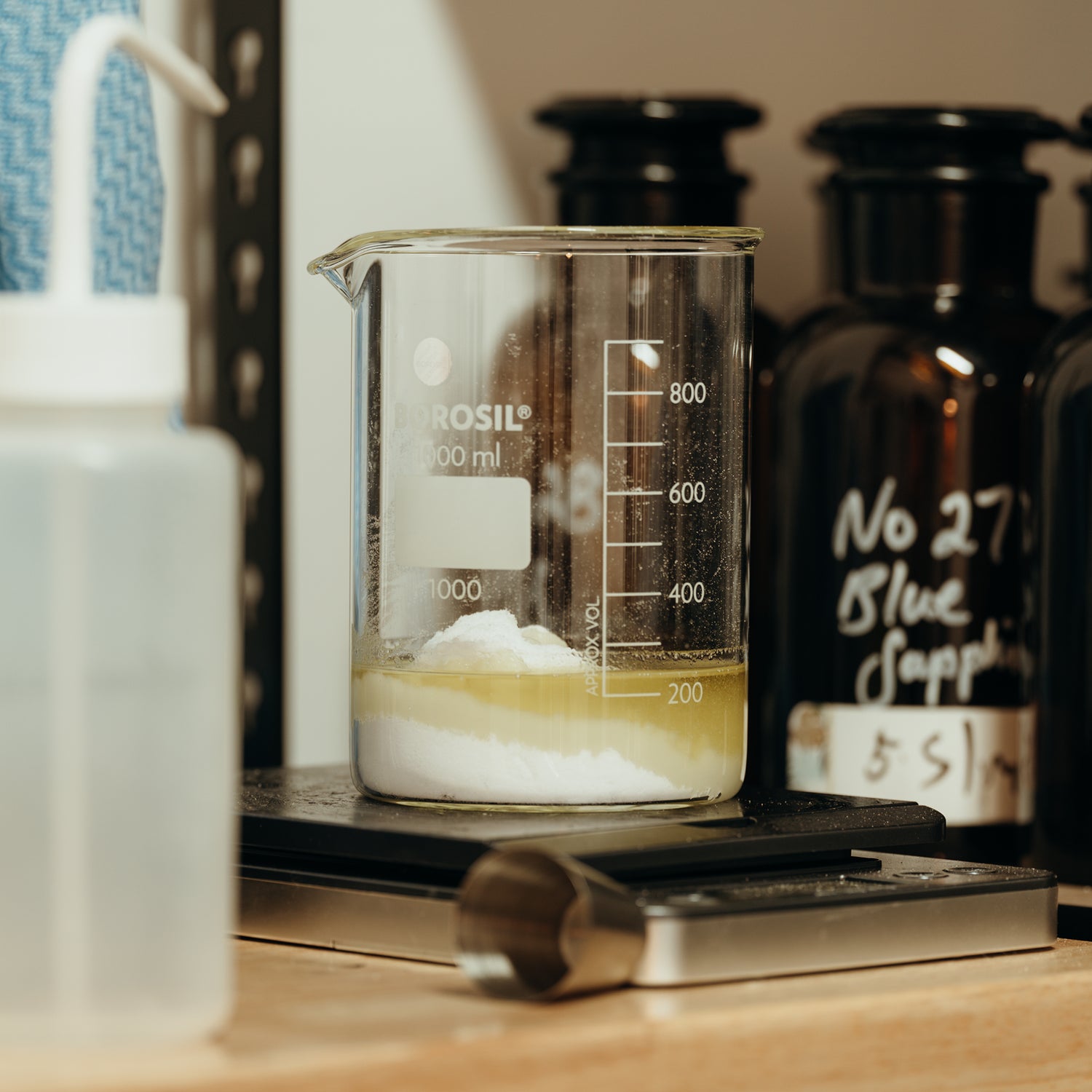 LeScent perfume lab beaker with layered fragrance base and powder ingredients during compounding process in workshop.