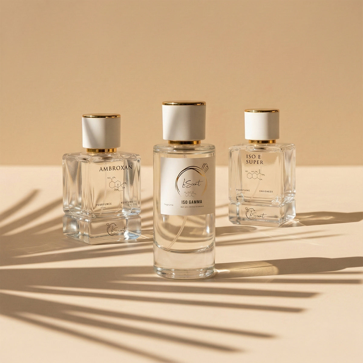 Three glass perfume bottles with white and gold caps sitting on a warm beige surface with cast palm leaf shadows, inspired by LeScent Ambroxan Perfume Primer, LeScent Iso Gamma Perfume Primer, and LeScent Iso E Super Perfume Primer.