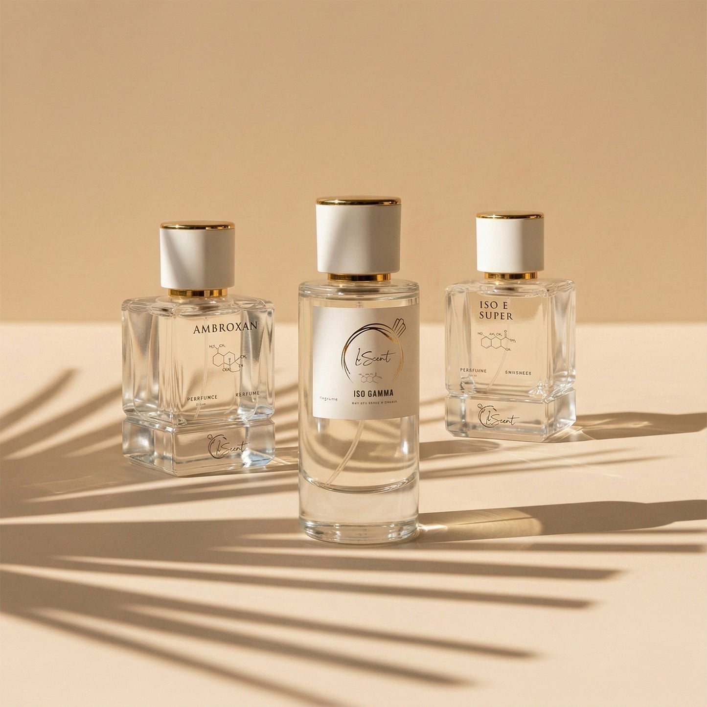 Three glass perfume bottles with white and gold caps sitting on a warm beige surface with cast palm leaf shadows, inspired by LeScent Ambroxan Perfume Primer, LeScent Iso Gamma Perfume Primer, and LeScent Iso E Super Perfume Primer.