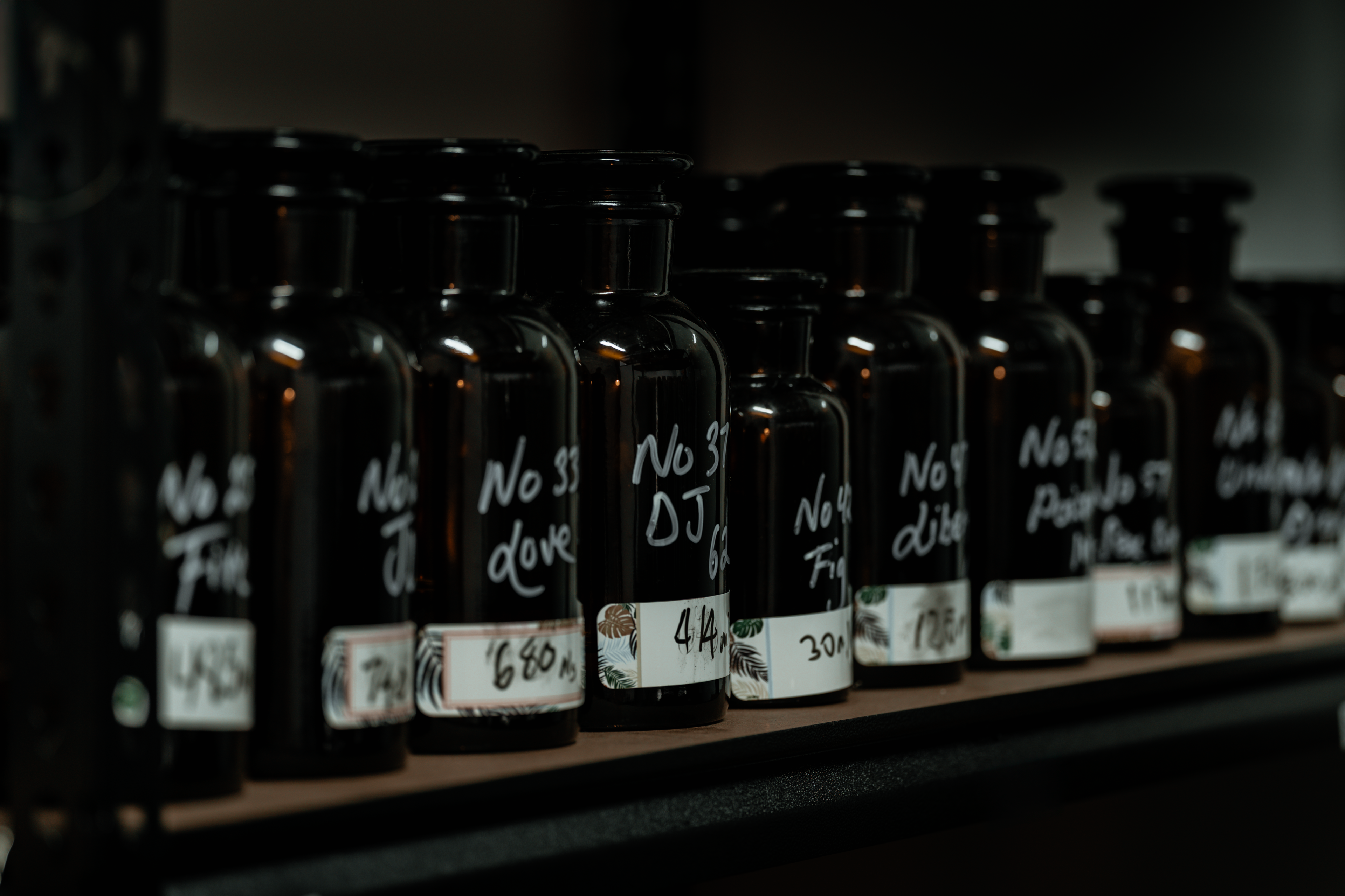 Close-up view of black glass fragrance bottles with handwritten labels in a perfumer’s workshop — showcasing raw essence storage for LeScent’s handcrafted scents.