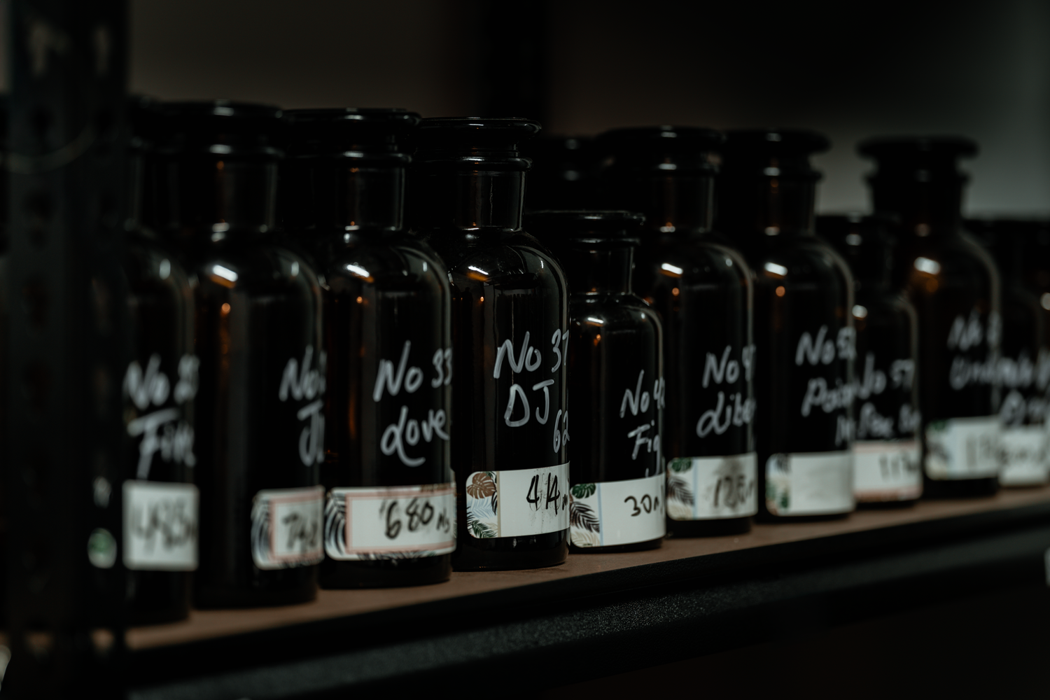 Close-up view of black glass fragrance bottles with handwritten labels in a perfumer’s workshop — showcasing raw essence storage for LeScent’s handcrafted scents.