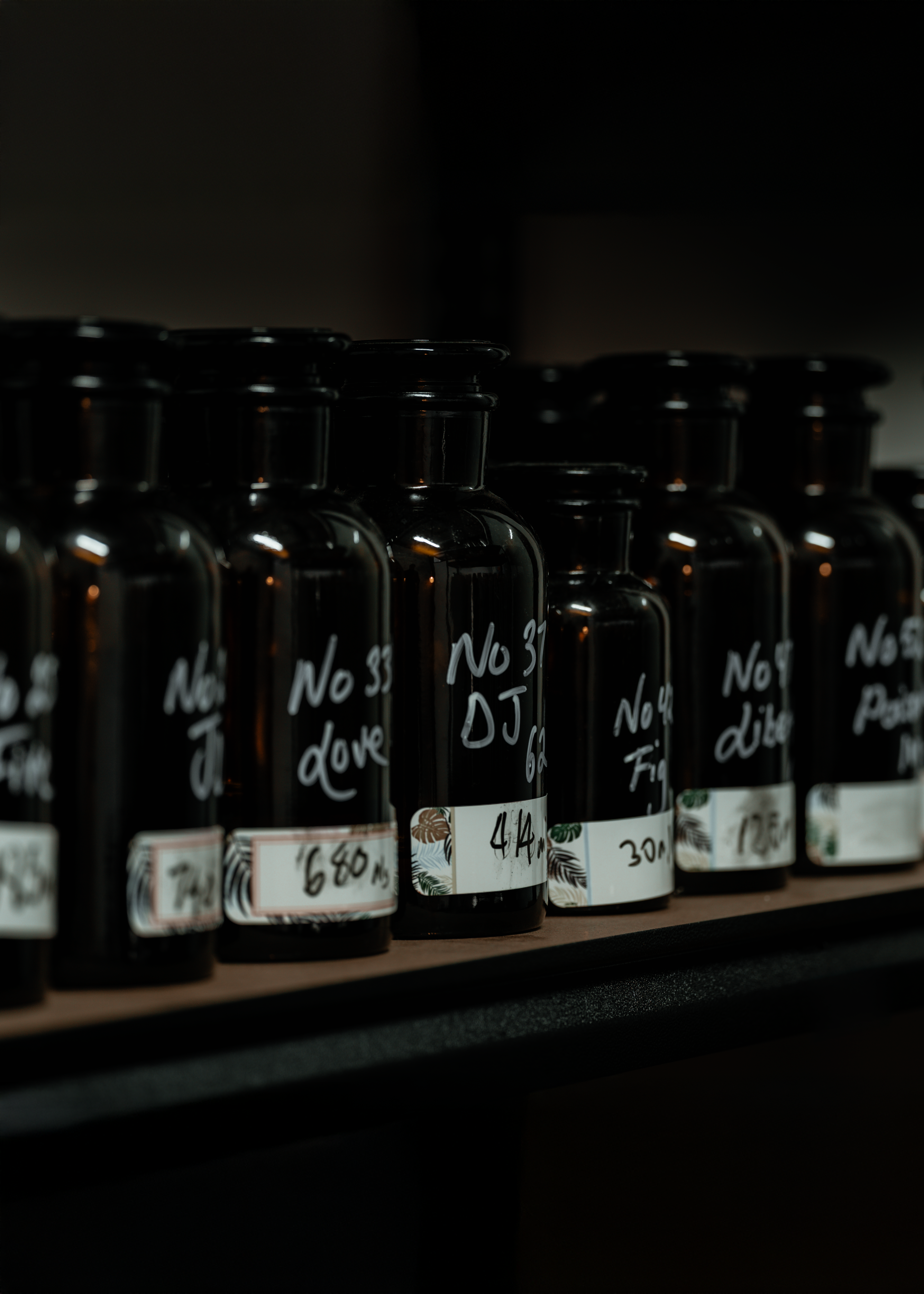 Dark amber perfume ingredient bottles lined up on a shelf inside a fragrance lab — artisanal perfume oils used in handcrafted LeScent formulations.