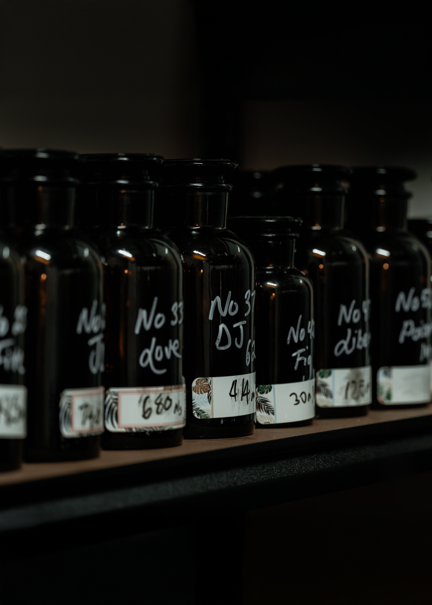 Dark amber perfume ingredient bottles lined up on a shelf inside a fragrance lab — artisanal perfume oils used in handcrafted LeScent formulations.