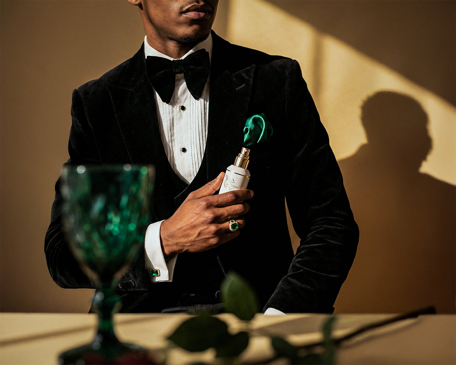 Man in a black tuxedo holding LeScent room spray with emerald accessories, luxury lifestyle image for home fragrance and room freshener.
