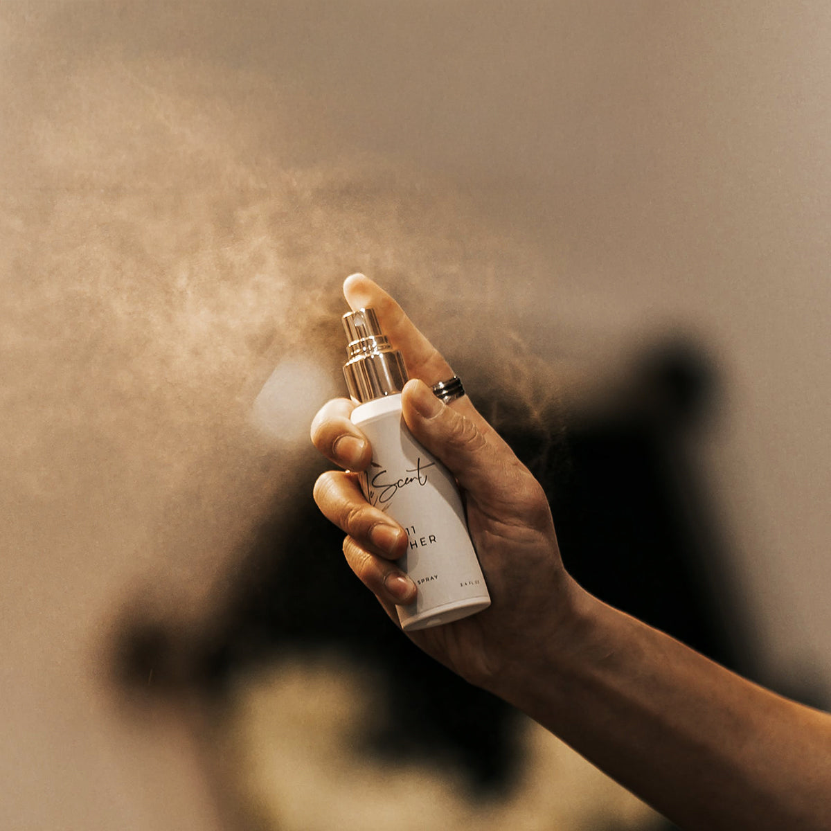 Hand spraying LeScent room spray into the air, home fragrance spray and room freshener in a close-up lifestyle image.