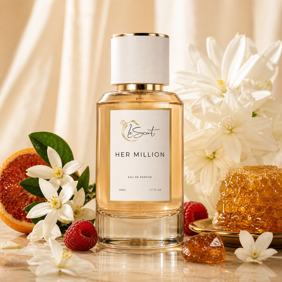 A bottle of HER MILLION Eau de Parfum by LeScent, filled with golden amber liquid, set on a reflective surface surrounded by white flowers, a sliced grapefruit, raspberries, and a honeycomb piece against a draped cream fabric background.
